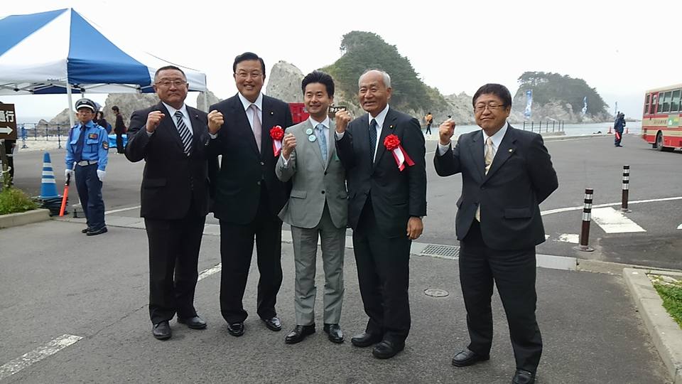右手の握りこぶしを胸の高さまで上げたポーズをとる市長と4名の男性の記念写真