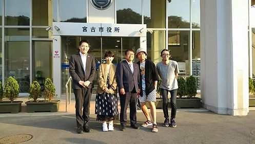宮古市役所の入り口の前で並んで記念撮影をする市長と台湾のロックバンド「Fire EX.」のボーカルSAMさん、関係者の方3名の写真