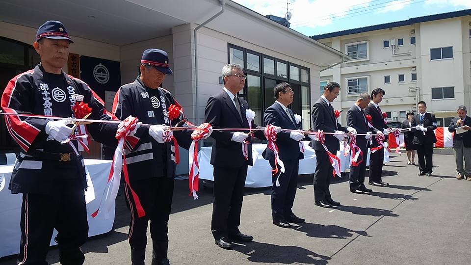 スーツを着た市長と関係者の男性4名と、法被を着た消防団員2名がテープカットしようとしている写真