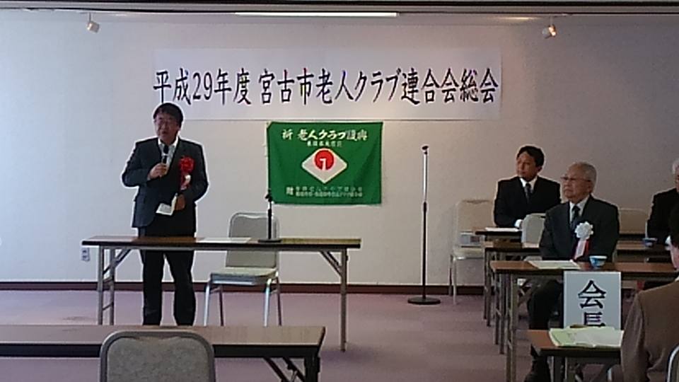「平成29年度宮古市老人クラブ連合会総会」と書かれた紙が貼られた壁の前で、右手にマイクを持って話をする市長の写真