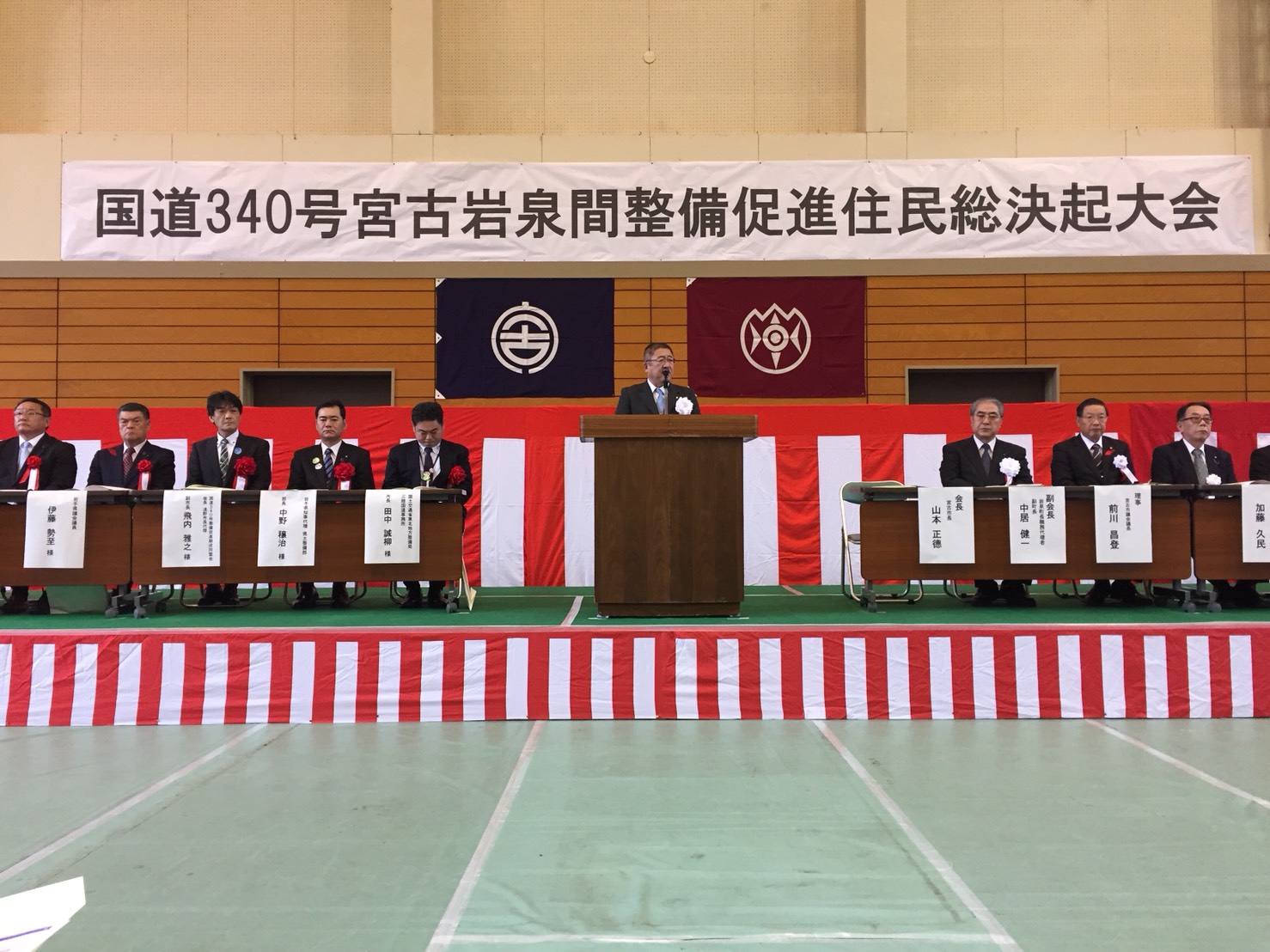 「国道340号宮古岩泉間整備促進住民総決起大会」と書かれた横断幕の下で、演台に置かれたマイクに向かい話をする様子の市長の写真