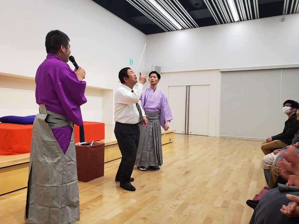 袴を着た2人の男性の間で曲芸に挑戦する様子の市長の写真