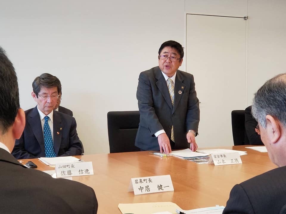 テーブルに向かい合って座る関係者3名と、テーブルの上の資料に手を添えて立って話をしている様子の市長の写真