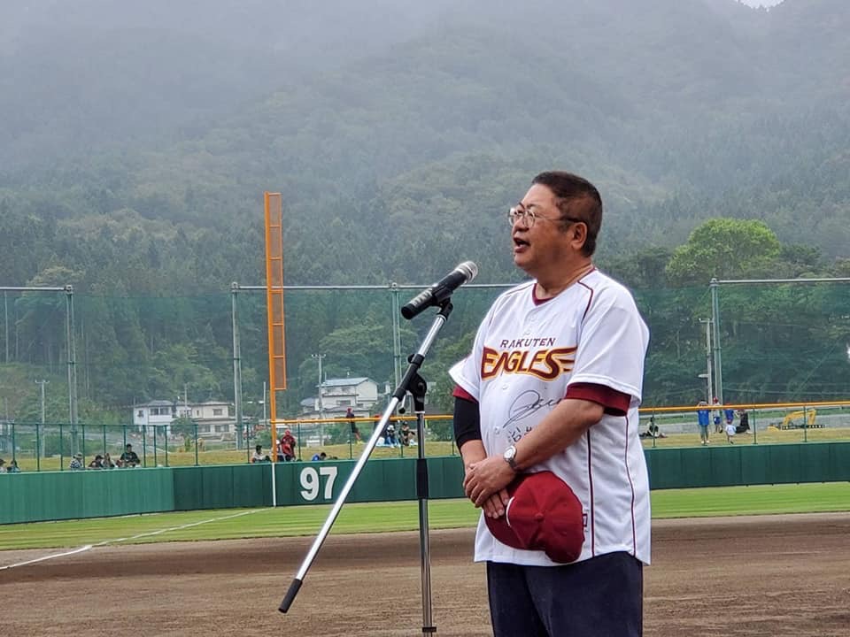 野球場で東北楽天ゴールデンイーグルスのユニフォームを着てスタンドマイクに向かい話をする様子の市長の写真
