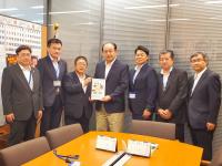 市長を含む男性7名が机の角に沿って並んで立ち、市長と男性で要望書を持っている写真