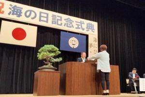 「海の日記念式典」と書かれたボードが吊るされたステージ上の演台で、市長が功績を挙げられた方に賞状を渡している写真