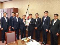 国旗が置いてある机の前で、市長を含む男性8名が並んで立ち、市長と男性で要望書を持っている写真