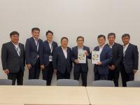 椅子が並んでいる部屋で、市長を含む男性8名が並んで立ち、男性2名がそれぞれ要望書を持っている写真