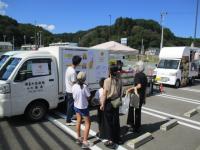 親子連れが駐車場に並ぶキッチンカーを見ている写真