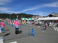 青空の下、摂待七つ物を踊る人達と、椅子に座り観覧する人達の写真