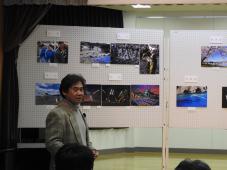 展示パネルに展示された作品を背に立っている審査員の男性が話しをしている様子を撮影した写真