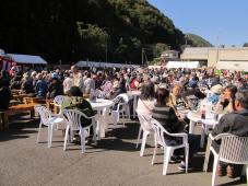 白いテントが見える手前にたくさんの人が丸いテーブルと椅子に座ってイベントを見学している人たちの様子を撮影した写真