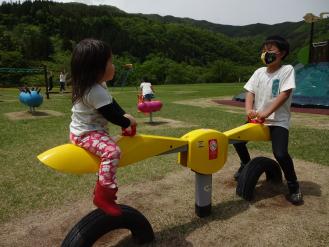 プロペラの形をした黄色のシーソーの奥に男の子、手前に女の子が乗っている写真