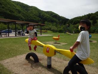 プロペラの形をした黄色のシーソーの奥に女の子、手前に男の子が乗っている写真