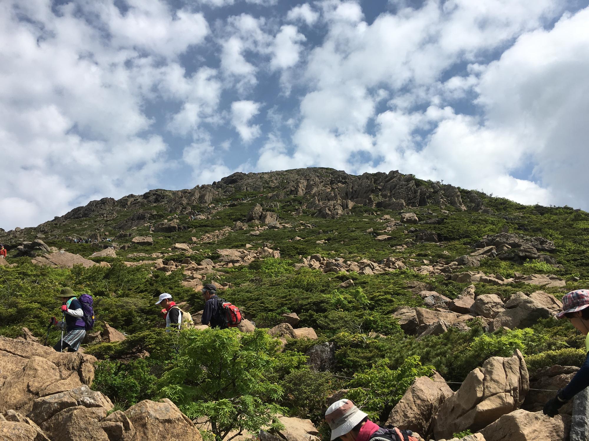 山頂を目指し早池峰山を登り始めた人々が手前に見える、早池峰山の山全体を麓から見上げた写真
