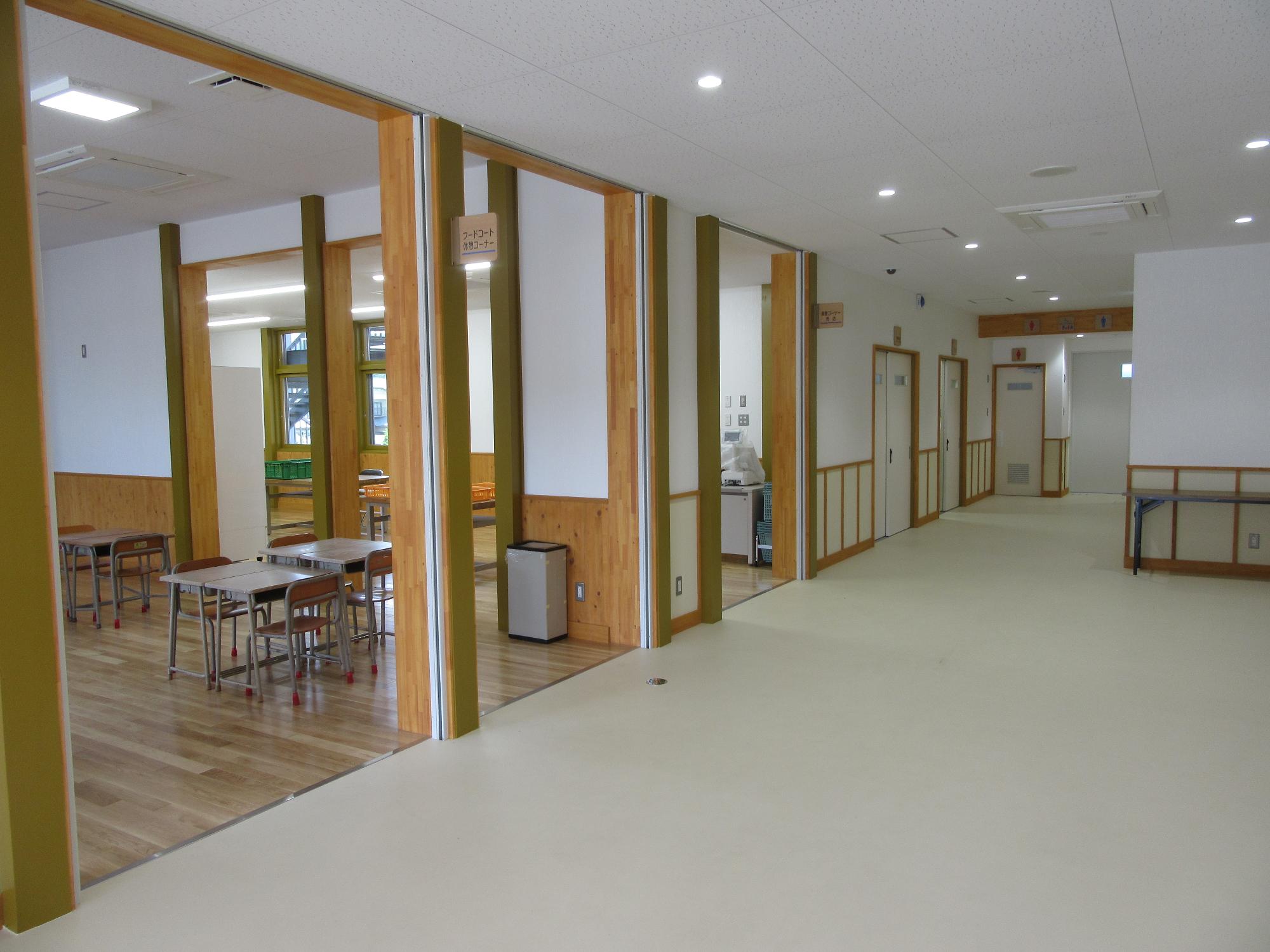 左側3つに仕切られた大きな入口の手前の1つから学校で使用されていた机といすが2組と奥に1組見える様子を撮影した写真