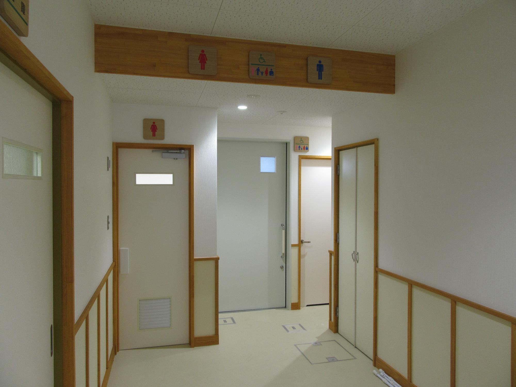 左の扉が女性用、中央が多目的トイレ、右奥へ続く男性用トイレの入口の表示を撮影した写真
