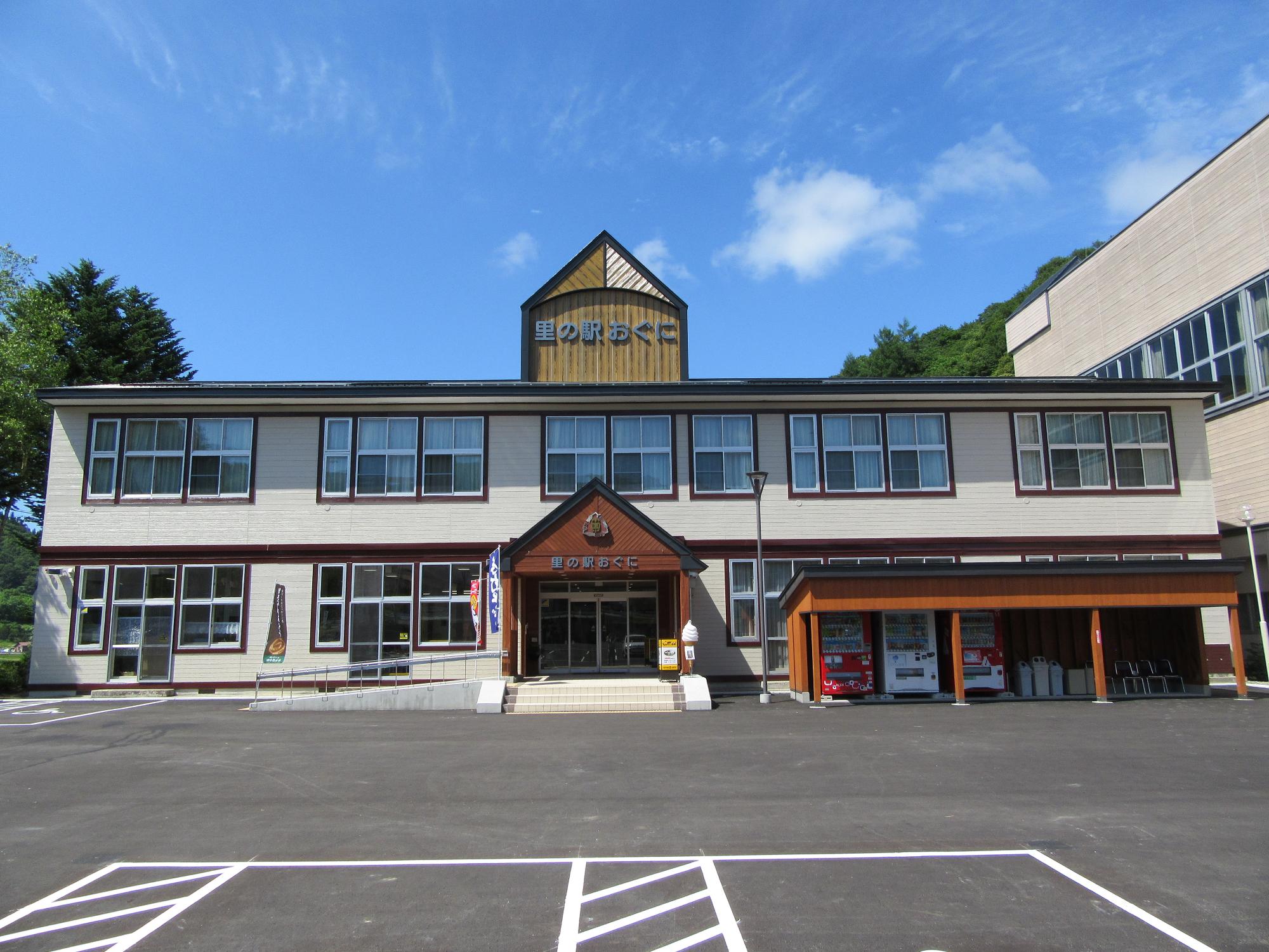 白く横長の2階建ての建物中央から突き出して見える三角の煙突のような看板と玄関の三角屋根の中央に里の駅おぐにと書かれた特徴的な外観を撮影した写真