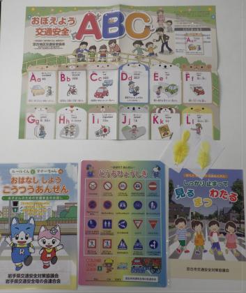 各種交通安全啓発リーフレット、交通安全下敷きそして黄色い羽がテーブルに置かれている写真