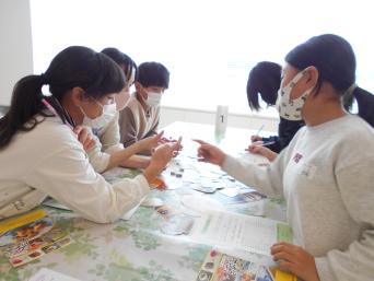 5人の子供たちが机に腕を伸ばし話し合いをしている写真