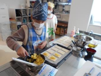 一人の子供が煮詰めたリンゴを上手にすくいシートにのせようとしている料理中の写真