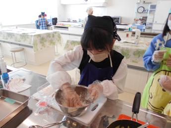女の子がボールの中のものをビニール手袋をした手で混ぜている写真