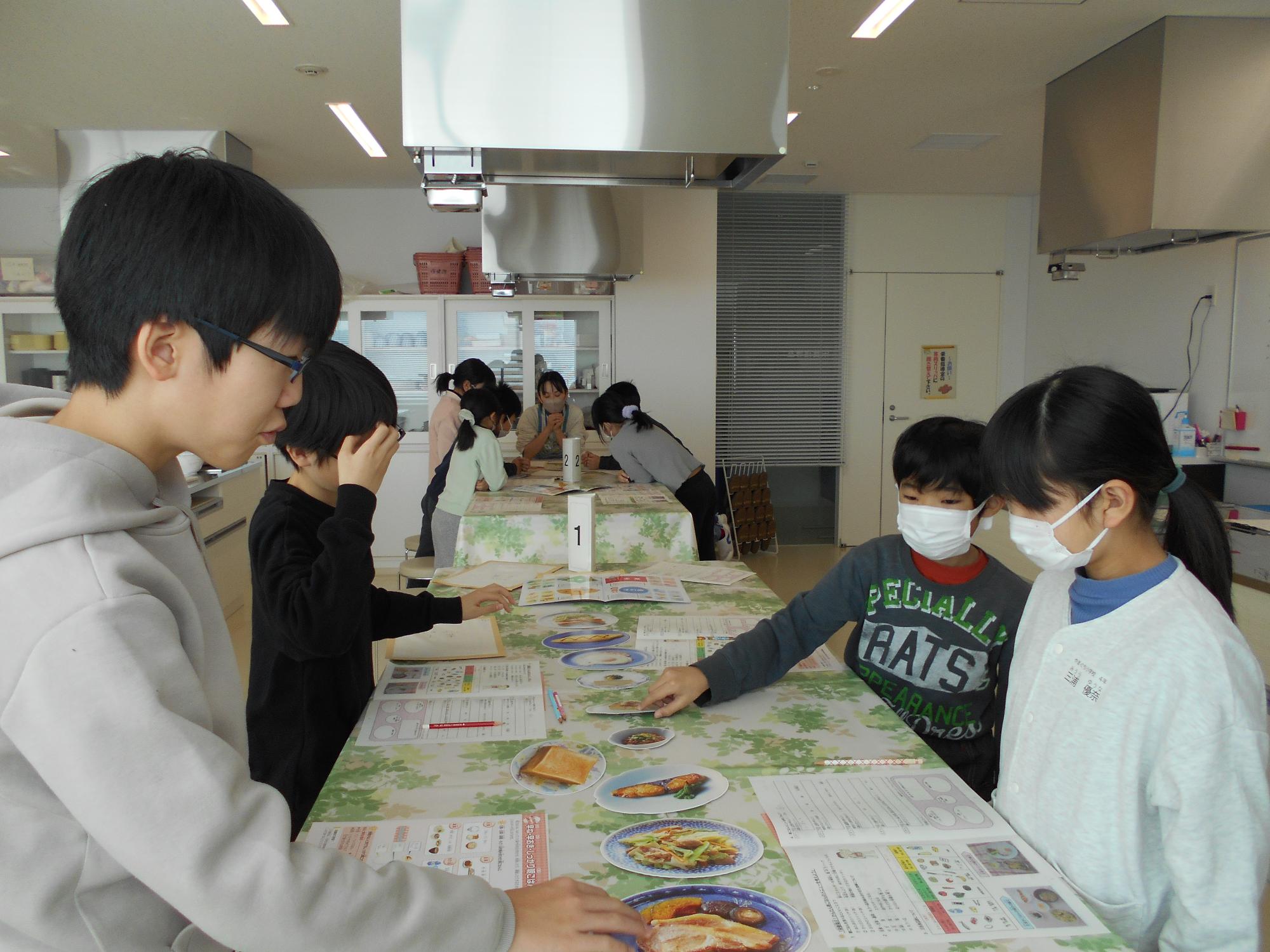 子ども4人が向かい合い料理の紙を広げている写真
