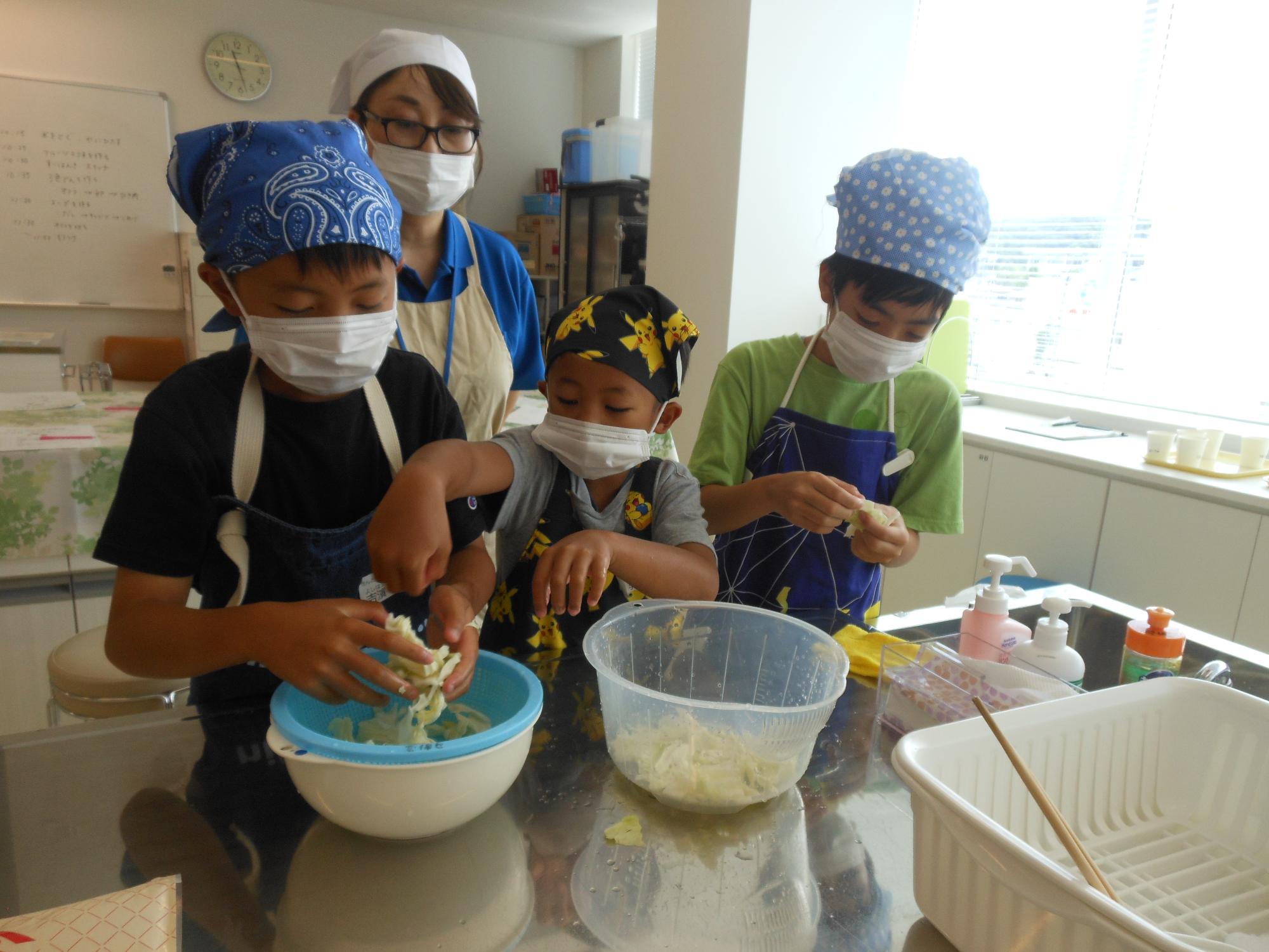 スープに入れるきゃべつをちぎっている男の子3人の写真