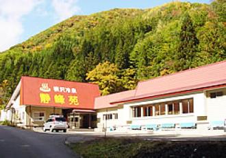 緑に囲まれ、赤い屋根に「横沢温泉 静峰苑」と大きく書かれた建物の外観写真