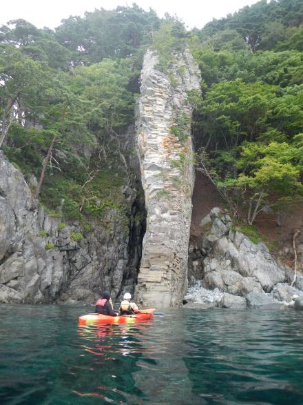 カヤックに乗りライフジャケットを着た2人が巨大なローソク岩を近くで見ている様子の写真