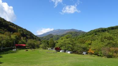 青空の下、奥には緑が綺麗な森や山が見える、芝地のタイマグラキャンプ場の写真