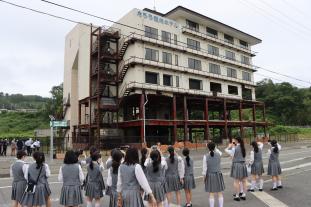 制服姿の高校生達が津波で被害を受けた、たろう観光ホテルを見ている様子の写真