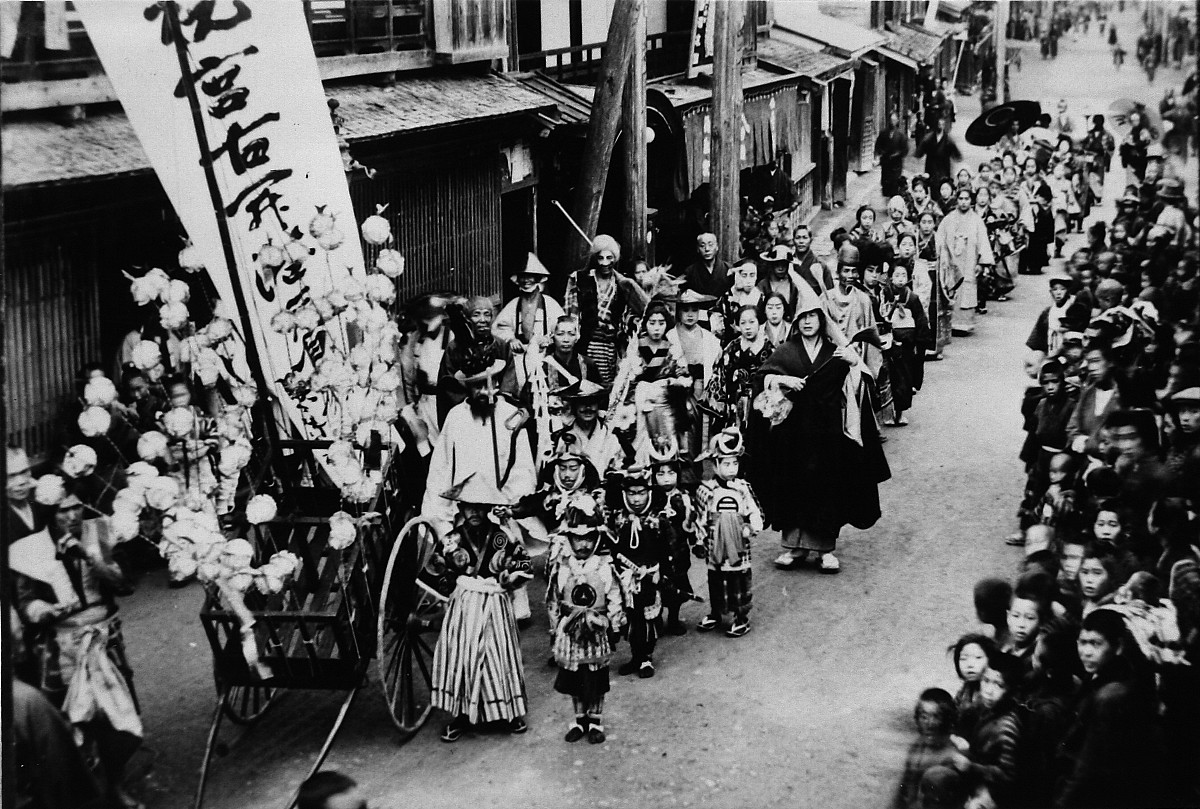 道の両脇にたくさんの民衆が並び、中央をお祝いの行列が通っている様子を写した白黒写真