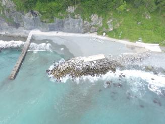 海に突き出た堤防と、たくさんのコンクリートのブロックが置かれた海岸がある港を上空から見た写真