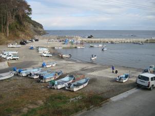 海に向かって8艘の船が陸に置かれるその先には作業用の車が停められていて右側に海へと伸びる防波堤を前方から撮影した写真