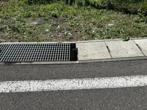 側溝にコンクリート製と金属製の二種類の蓋が置かれ、それぞれの蓋と蓋の間に数センチほどのすき間がある様子を写した写真