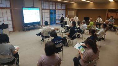 和室にパイプ椅子を並べ参加者の人たちが座り前方のスクリーンを見ている写真