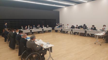 コ型に長机が並べられ左奥の男性が1人立っている会議室内の写真