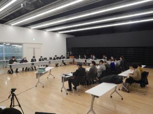 壁が白と黒のモノトーンの室内で白い長机をコ型に設置し、会議参加者が着席している写真