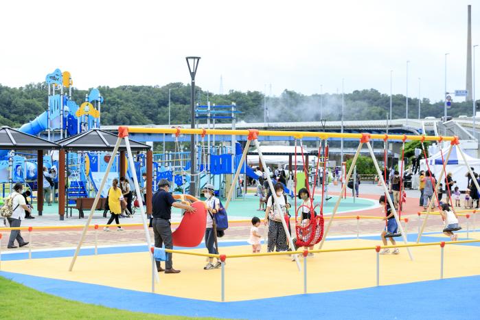 黄色や水色の色鮮やかな遊具がありたくさんの親子連れが遊んでいるうみどり公園の写真