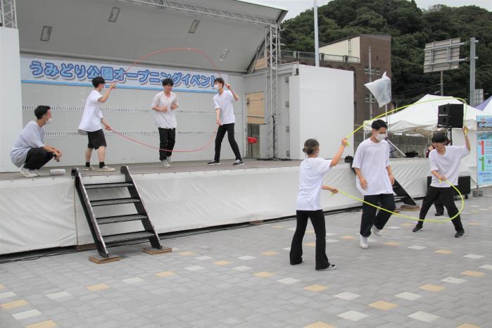 舞台の上と下で2名の人が二本の縄跳びを回しその間を1人がとんでいるなわとび競技をしている写真