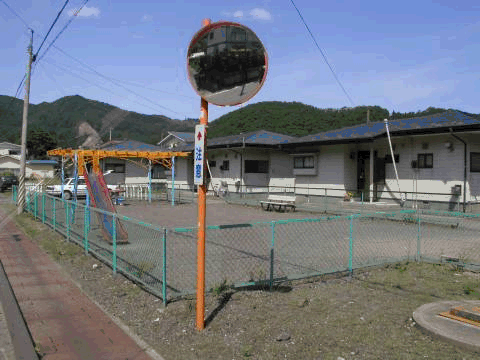手前にカーブミラーがあり、滑り台などの遊具が設置された児童遊園の写真