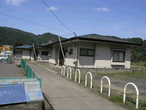 後ろに小高い山が見え、公園横に平屋建て戸建住宅が並んでいる外観写真