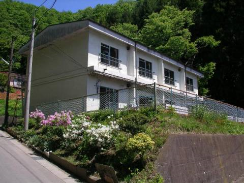 緑に囲まれ、坂道の横に建ってる2階建て長屋住宅の外観写真
