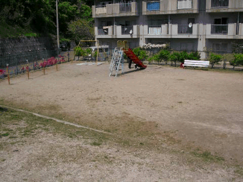中里団地住宅の前に滑り台やブランコ、鉄棒が設置された児童遊園の写真