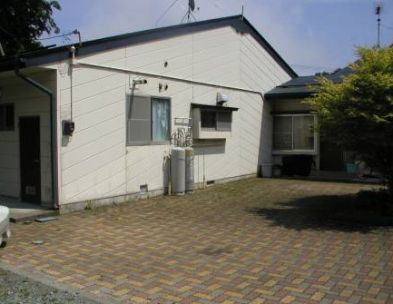 手前の一角に1本の木が立ち、白い外壁の長内団地住宅の外観写真