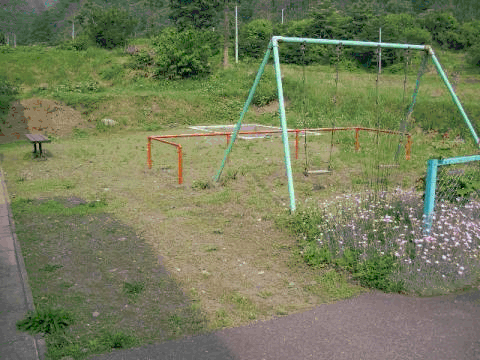 緑に囲まれ、ブランコが設置された刈屋日向団地住宅の児童遊園の写真