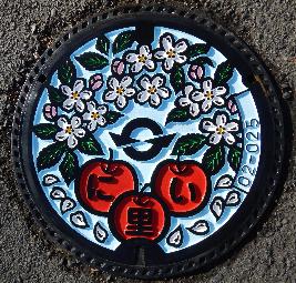 青空にリンゴとリンゴの花が描かれているマンホールの画像