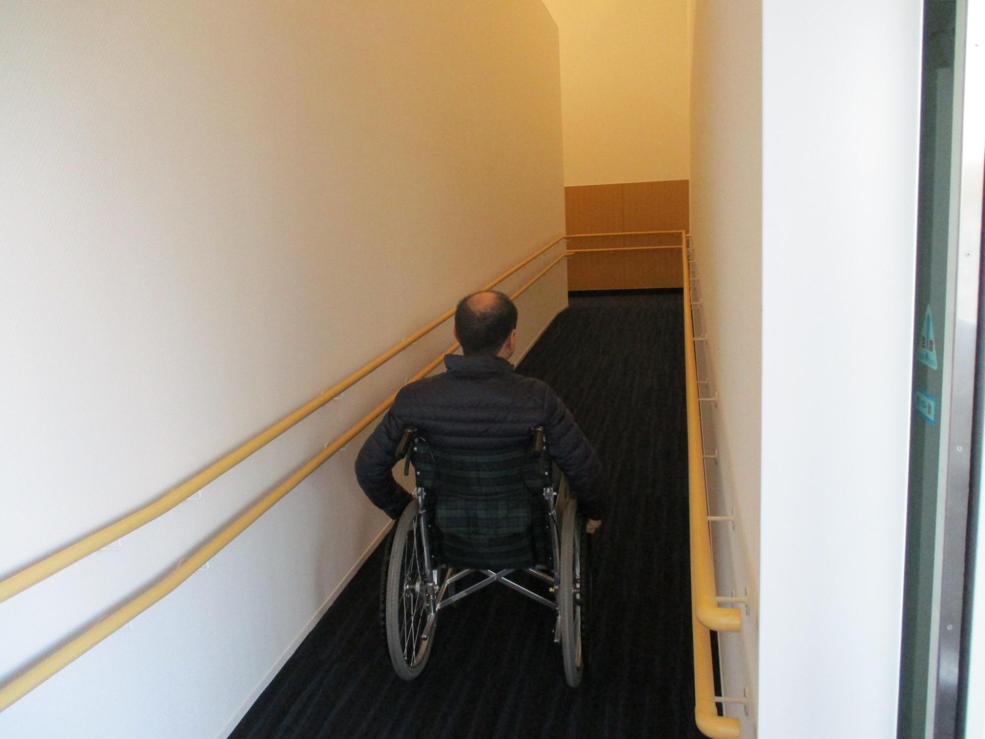 スロープを車いすに乗っている方が下っている写真