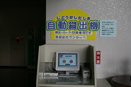 壁に「自動貸出機」と書かれた案内が貼られている真下に机の上に置かれている自動貸出機の写真